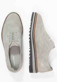 Šedé semišové boty s designem wingtip, zdobené složitými perforacemi, kontrastní černobílou podrážkou a přírodním koženým lemem.