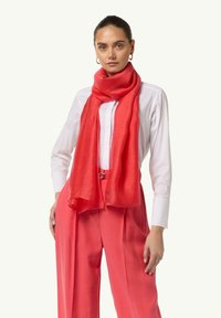 Jasnoczerwony szal z lekkiego, teksturowanego materiału, swobodnie opleciony wokół szyi, zestawiony z białą koszulą i różowymi spodniami.