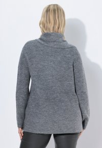 Grijze gebreide trui met een hoge kraag, losse pasvorm en lange mouwen. De stof heeft een zachte textuur en een iets oneffen zoom aan de achterkant.