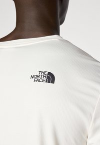 Close-up of a person wearing a white textured shirt with The North Face logo printed in black on the upper back.