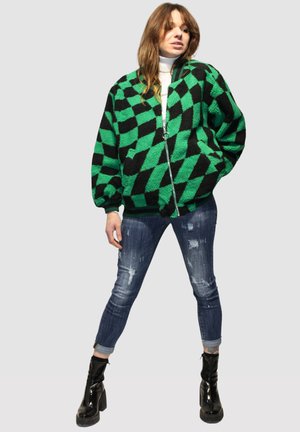 Chaqueta de forro polar a cuadros en negro y verde, con cierre de cremallera en el frente, puños y dobladillo acanalados. Combinada con jeans azules desgastados y botas negras de charol.