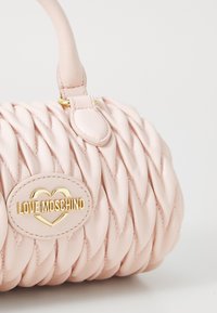 Pink braided handbag made of leather, featuring a gold-tone logo plaque and a rounded shape. Includes a short, structured handle.