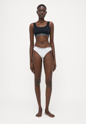 Zwarte crop topsportbeha met branding en witte hipster onderbroek met een logo tailleband; gladde stof en een strakke pasvorm.