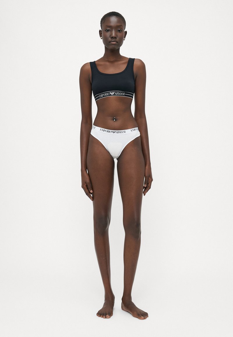 Soutien-gorge de sport noir court avec logo et culottes hipster blanches ornées d'une ceinture à logo ; tissu lisse et design ajusté.