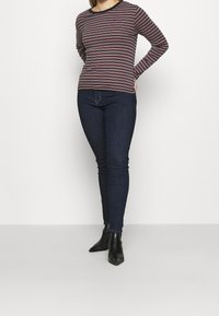 Camisa de manga larga a rayas en azul marino oscuro y burdeos, con un escote redondo y diseño ajustado, combinada con jeans ajustados azul oscuro y botines negros.