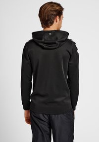 Felpa nera con cappuccio, maniche lunghe e tessuto testurizzato. Presenta un logo sulla parte posteriore e spalle con dettagli distintivi.