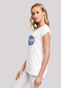 White cotton t-shirt with a round NASA logo in blue and red. Short rolled sleeves and a relaxed fit. Smooth texture and casual design.