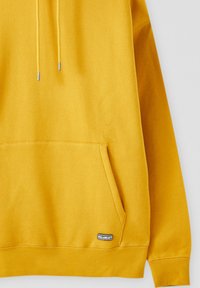 Sweat à capuche jaune avec poche kangourou à l'avant et petite étiquette rectangulaire avec le logo Pull&Bear au bord de la poche.