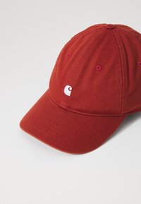 Piros pamut baseball sapka ívelt karimával, elöl fehér logóval, és varrott szellőző lyukakkal.