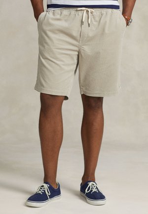 Khaki krótkie spodenki w paski wykonane z bawełny, wyposażone w elastyczny pas z sznurkiem, noszone z granatowymi casualowymi trampkami.