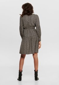 Schwarzes Blumenkleid mit langen Ärmeln, taillierter Taille und schichtmäßigem Rock, das ein dezentes Muster und einen leichten, strukturierten Stoff aufweist.