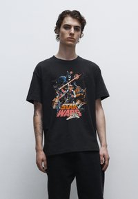 Černé bavlněné tričko s barevným potiskem "Hvězdné války" zobrazujícím postavy a lodě, s uvolněným střihem a krátkými rukávy.