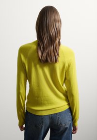Maglione verde lime con collo a giro e maniche lunghe, dotato di polsini e orlo a coste, abbinato a jeans a vita alta blu scuro.