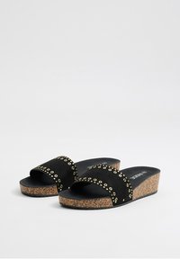 Sandalias de ante negro con acentos de ojales dorados, diseño de punta abierta y suela de cuña de corcho. Suela texturizada para un mejor agarre.