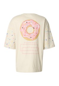 Krémové tričko s krátkým rukávem, na zádech velký růžový grafický motiv koblihy, na rukávech barevné posypky a pod ním minimální množství textu.