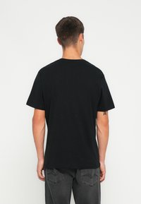 Camiseta de algodón negra con cuello redondo, mangas cortas y un corte holgado. La parte posterior revela un detalle mínimo y una textura suave.