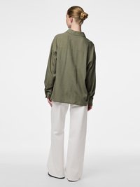 Olijfgroene, oversized shirt van lichtgewicht stof met een kraag, gecombineerd met witte wijde broekspijpen, wat zorgt voor een relaxte pasvorm en rugnaaddetail.