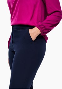Pantalon ajusté bleu marine avec poches latérales, associé à un chemisier rose vif aux manches amples et à la texture lisse.