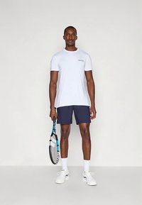 Valge lühikeste varrukatega spordisärk, tumesinised lühikesed püksid, tennisereket käes, valged jalanõud jalas. Lihtne disain, kerge kangas, vaba lõige.