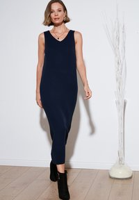 Abito a maglia a coste blu navy con scollo a V, silhouette aderente, lunghezza a metà polpaccio e spacco laterale. Abbinato a stivali neri alla caviglia.