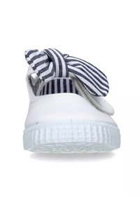 Sneaker bianco con suola texturizzata, caratterizzato da un nodo in tessuto a righe blu e bianche nella parte superiore. Design semplice, forma con punta chiusa.