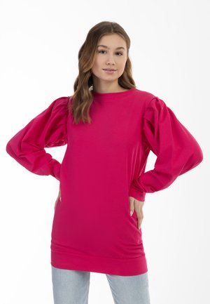 Fuchsia oversized sweatshirt met verzamelde ballonsleeves en een ronde hals, gemaakt van zachte stof, gecombineerd met lichtblauwe spijkerbroek.