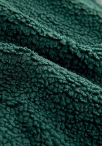 Tissu vert foncé texturé avec une surface moelleuse et surélevée. Le matériau semble doux, idéal pour la chaleur et le confort.