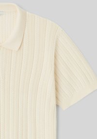 Polo shirt tricoté à manches courtes couleur crème avec texture de côtes verticales et motif de feuilles subtil, arborant un col et des poignets doux.