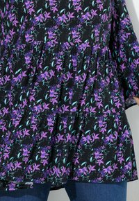 Black garment featuring a floral design with purple flowers and teal leaves. The fabric has a textured appearance and a gathered hem.