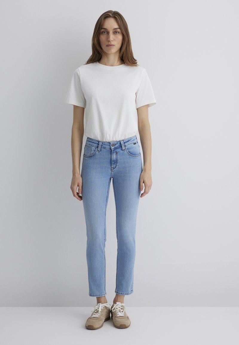 Light blue denim jeans with a slim fit and ankle-length cut, paired with a plain white cotton t-shirt and beige sneakers.