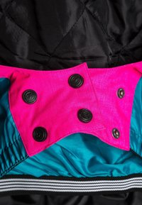 Nahaufnahme einer schwarzen, gesteppten Stoffjacke mit gestreiftem Bündchen, die einen rosa Druckknopfverschluss über einem türkisfarbenen Futter zeigt.