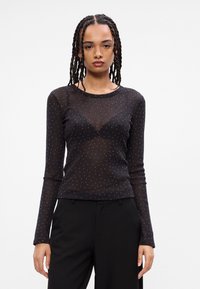 Top negro transparente de manga larga con sutiles puntos brillantes, diseño ajustado, cuello redondo y tejido texturizado. Combinado con pantalones negros.