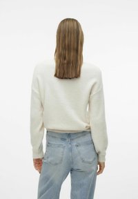 Pull en maille de couleur claire, avec une coupe décontractée, des poignets côtelés et un col rond. Associé à un jean taille haute bleu clair.