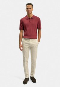 Burgundy ribbade polo skjorta med krage, matchad med beige skräddarsydda byxor och mörkbruna skor. Tyget verkar mjukt och texturerat.