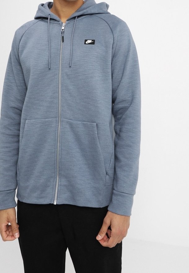 Světle modrá mikina na zip s texturovaným povrchem, kapuce se stahovací šňůrkou, přední kapsy a malé černé logo Nike na levé hrudi.