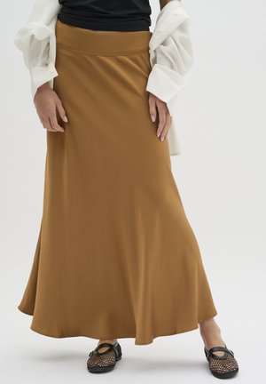 Brun maxiskørt med en bred talje, glat tekstur og en let flædret silhuet. Båret med sorte net-sko og en hvid oversized skjorte.