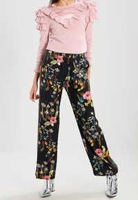 Haut rose clair à manches longues avec un col à volants ; pantalon palazzo noir à fleurs présentant des couleurs comme le rose, le jaune et le vert ; bottes argentées brillantes.