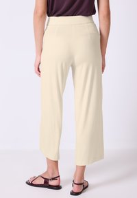Licht beige wijde broek met een gladde stof, elastische tailleband en twee achterzakken; gecombineerd met donkerbruin sandalen.