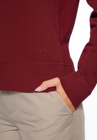 Bordeauxfarbener Sweatshirt mit strukturiertem Strickdesign, gerippten Bündchen und Tasche. Dezente Logo-Stickerei am unteren Saum.