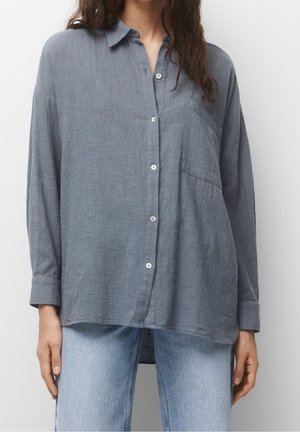 Grå skjorte med knapper, lange ærmer, tekstureret stof, brystlomme og buet kant, kombineret med lyseblå jeans.