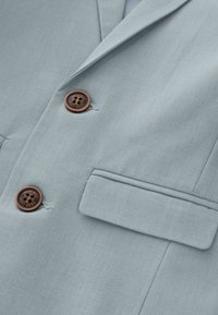 Lichtblauwe blazer met een textuurstof, twee bruine knopen en één borstzak. Gladde revers en strakke lijnen.