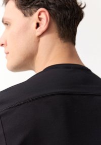 Czarna koszulka z krótkim rękawem i okrągłym dekoltem, wykonana z gładkiego materiału, z widocznymi szwami na ramionach i dekolcie.