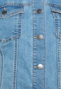 Jeans jakna u svijetloplavoj boji, klasičnog ovratnika, s dva džepa na prsima i srebrnim zakovicama duž prednje strane.