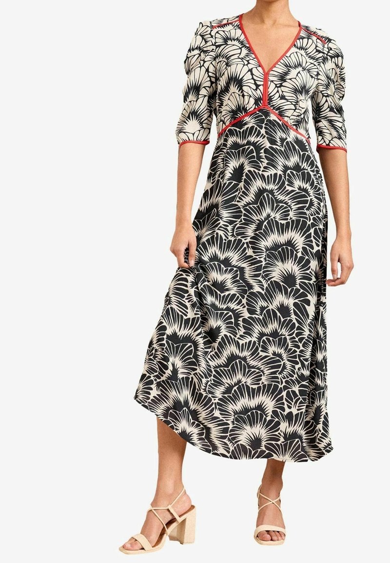 Svart och vit blommönstrad klänning med V-ringning, puffärmar, röda detaljer och en flödande A-linjeform. Matchad med beige blockklackssandaletter.