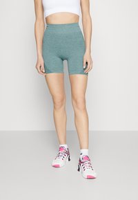 Turkosa, höga träningsshorts med ribbade detaljer nära nederkanten. Bärs med vita sneakers prydda med ett färgglatt mönster.