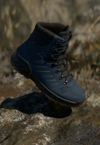 Hoge wandelschoen in marineblauw synthetisch materiaal met rubberen zool. Beschikt over een vetersluiting, gevoerde kraag en subtiele textuurmarkeringen.