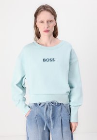 Světle modrá mikina s volným střihem, kulatým výstřihem a žebrovanými manžetami, s texturovaným logem "BOSS" uprostřed.