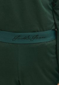 Roheline puuvillane rõivas, millel on pehme tekstuur ja elastne vöökoht, millel on musta kiri "Jack & Jones".