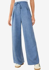 Pantalones de pierna ancha en azul claro, hechos de una tela texturizada, con un cinturón anudado y detalles de pliegues en la parte delantera, combinados con zapatillas blancas.