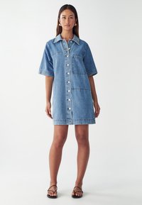 Denim jurk met korte mouwen, knoopsluiting aan de voorkant en een patchzak. Lichtblauwe kleur en een gladde textuur, halverwege de bovenbenen.